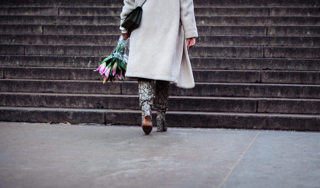 Bottom half of woman with flowers wearing a coat about to go up stairs