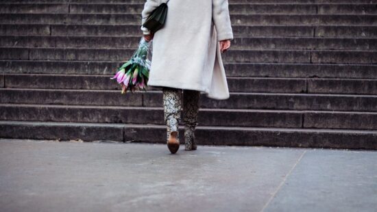 Bottom half of woman with flowers wearing a coat about to go up stairs